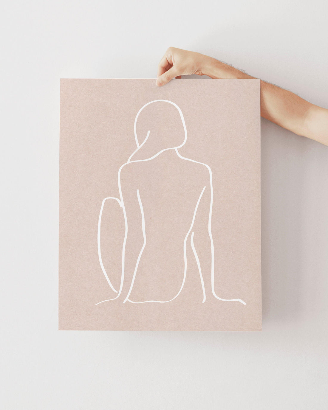 arm holding a print of a sketch of a girl sitting. white sketch on pink paper