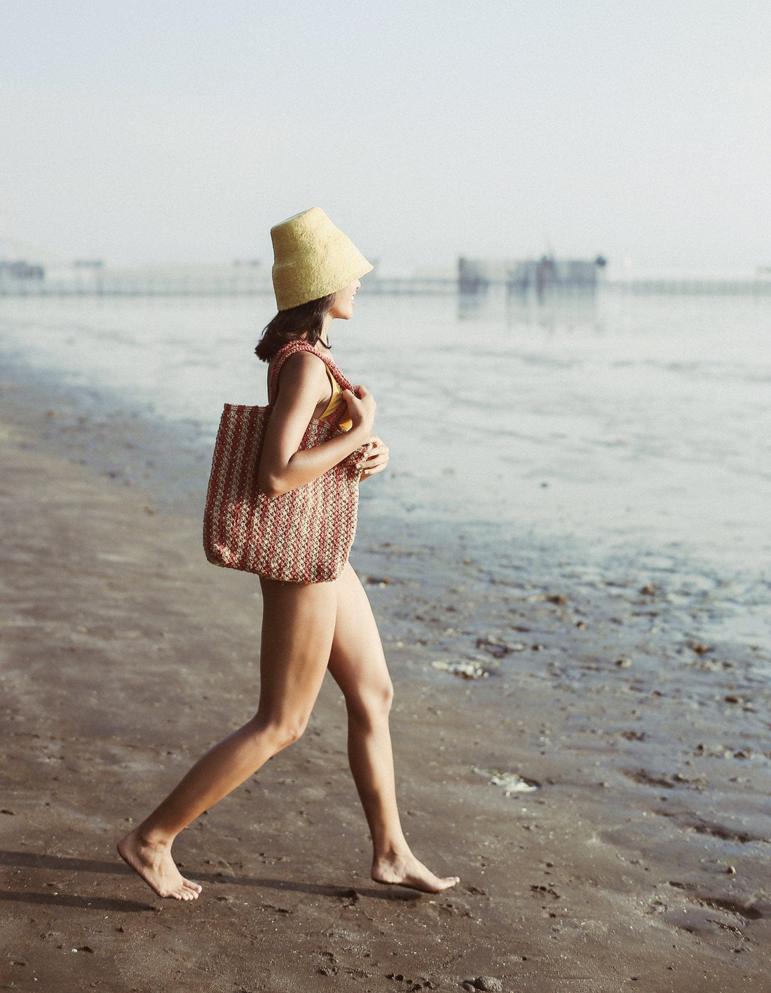 woman running on beach with bucket hat and striped jute tote